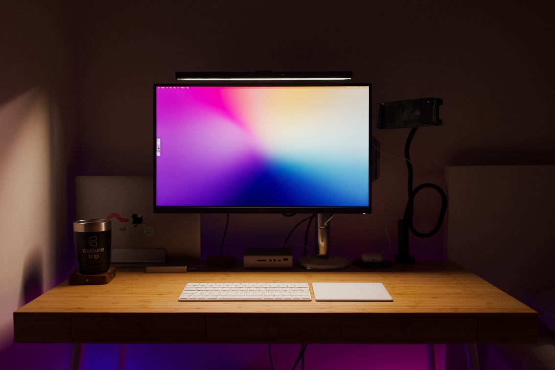 A photo of my current desk setup. A 3 draw wooden desk with a laptop, bluetooth speaker, coaster, trackpad, keyboard, magnetic cable tidy, Thunderbolt 3 dock, monitor arm holding up a 25" Ultrasharp and my iPhone X hoisted up on a gooseneck for webcam use.